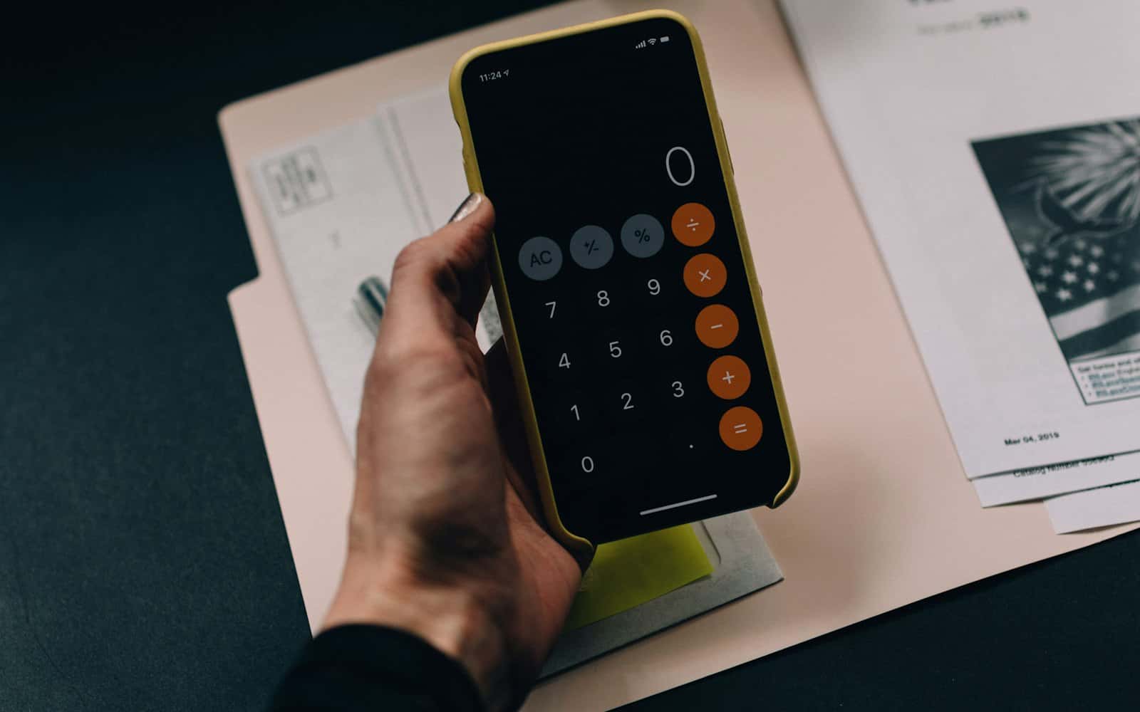 Belgelerin üzerinde telefonun hesap makinesiyle hesap yapan el