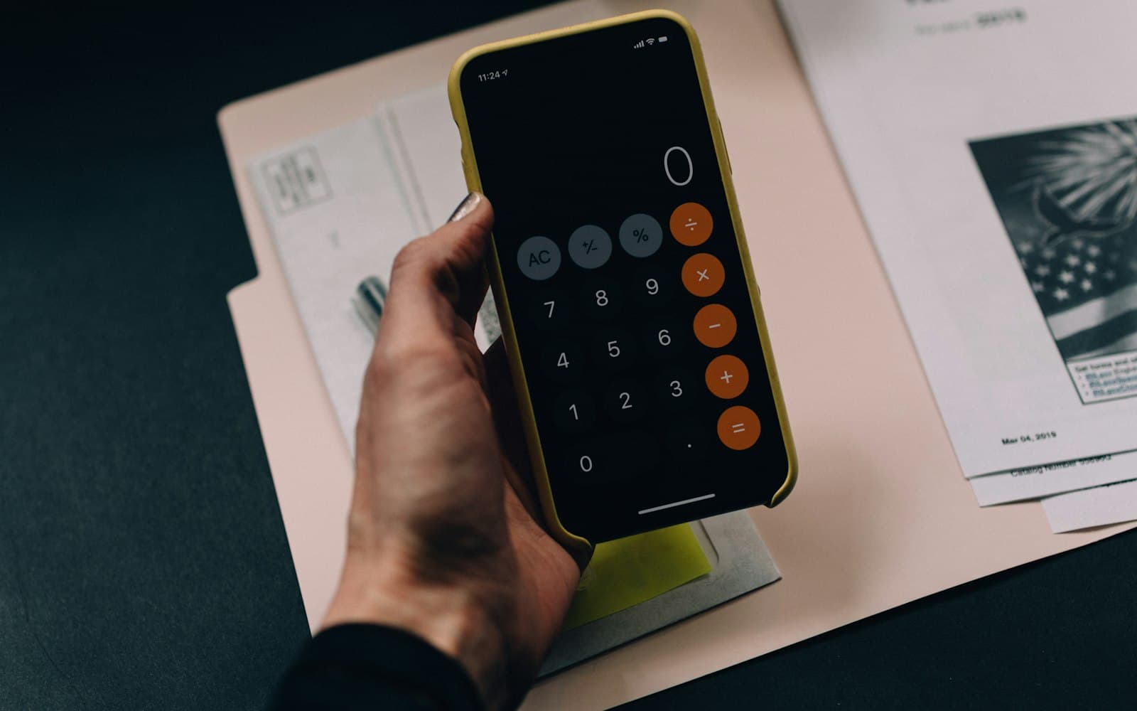 Belgelerin üzerinde telefonun hesap makinesiyle hesap yapan el